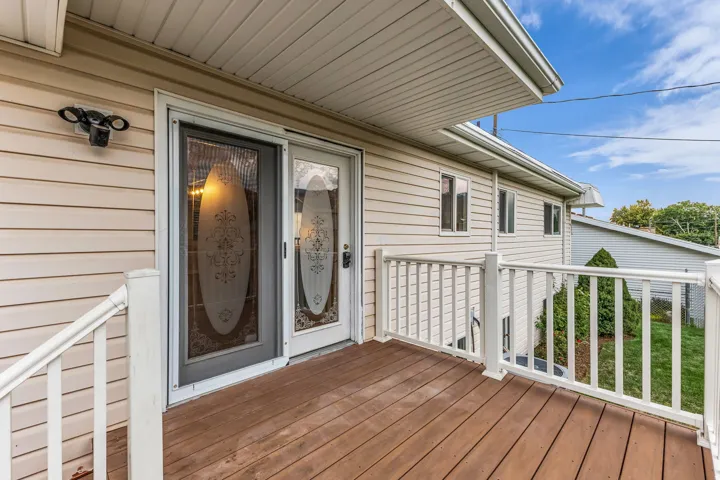 Wood-finish deck with white railing, featuring a glass-paneled storm door and a main entry door with decorative glass inserts