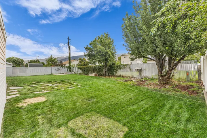 Expansive backyard featuring a manicured lawn, established trees, and a partial paver pathway