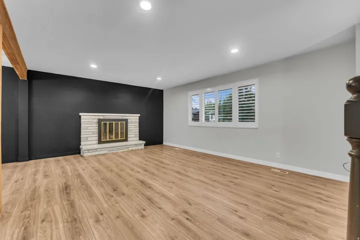 Wood-finish flooring throughout, recessed lighting, and a stone-clad fireplace with a dark accent wall