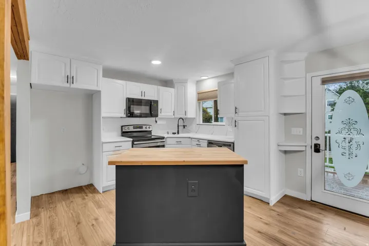 Kitchen featuring white cabinetry, wood-finish flooring, a butcher block island, black appliances, and white countertops