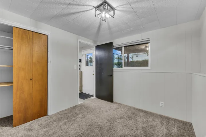 Carpeted flooring, paneled wall detail, wood-finish closet doors with shelving, recessed window, and a ceiling-mounted light fixture