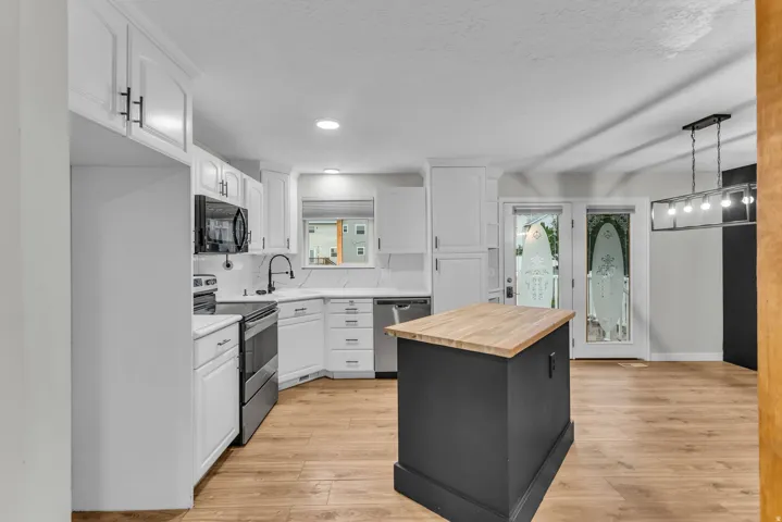 White cabinetry with matte black hardware, stainless steel appliances, wood-finish flooring, kitchen island with wood countertop, and double glass-paneled doors