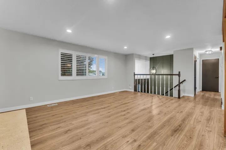 Wood-finish flooring, white plantation shutters, recessed ceiling lighting, staircase with a dark wood handrail, and a contemporary pendant light fixture