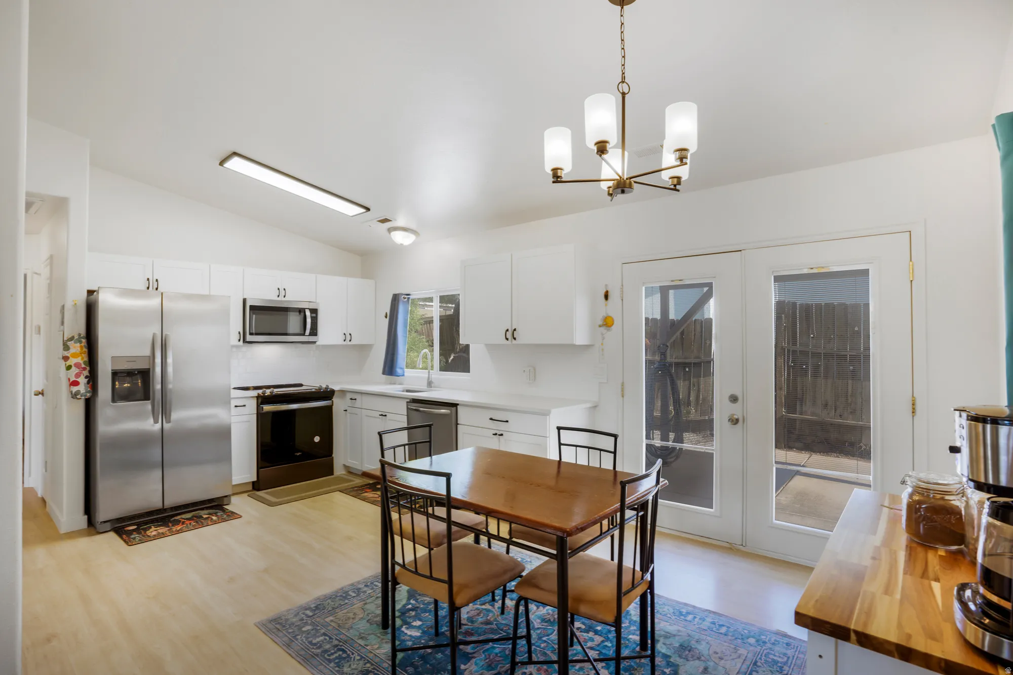 White cabinetry with stainless steel appliances, wood-finish flooring, and a contemporary chandelier
