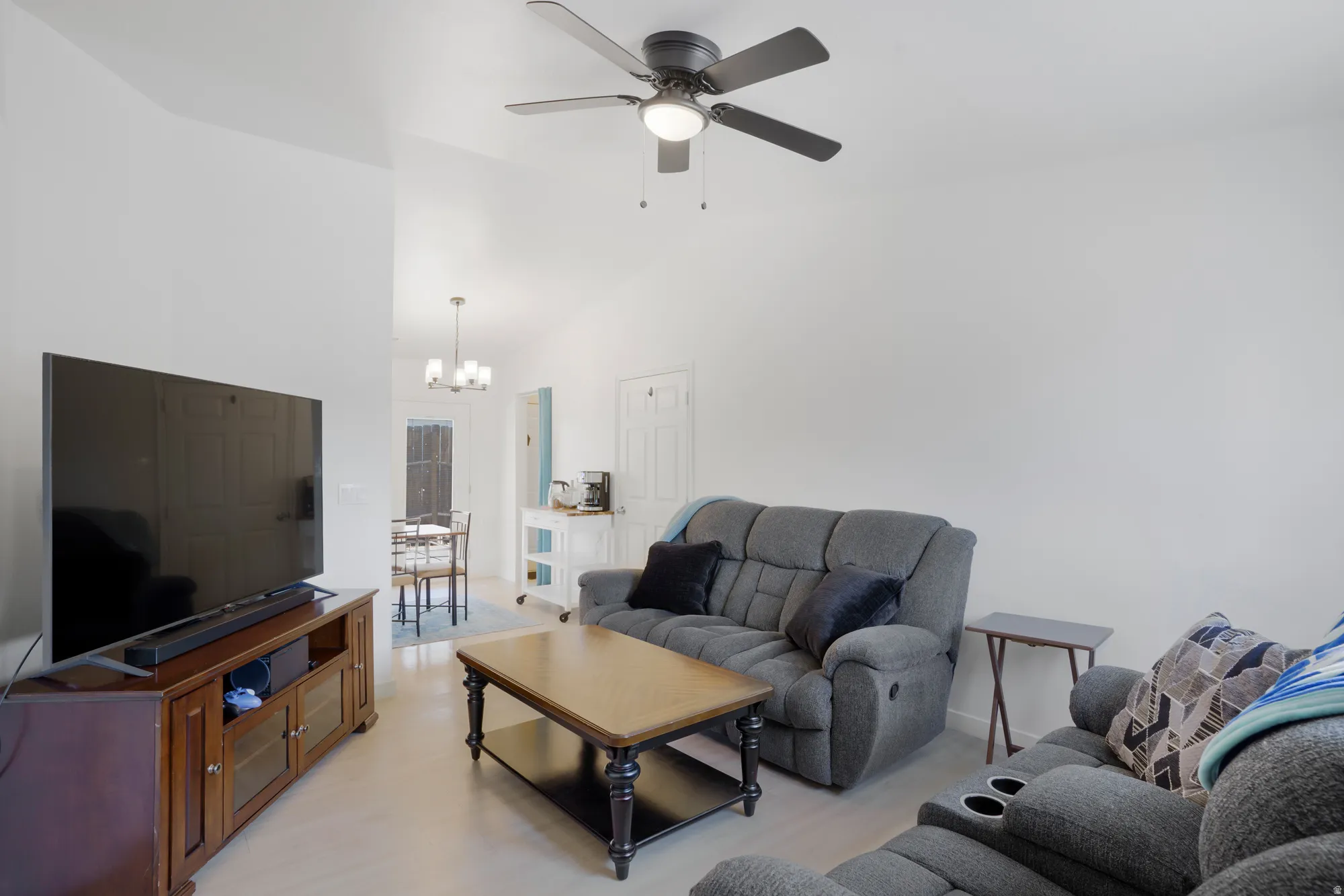 Vaulted ceilings with a ceiling fan, light-toned flooring, and a dining area with a chandelier