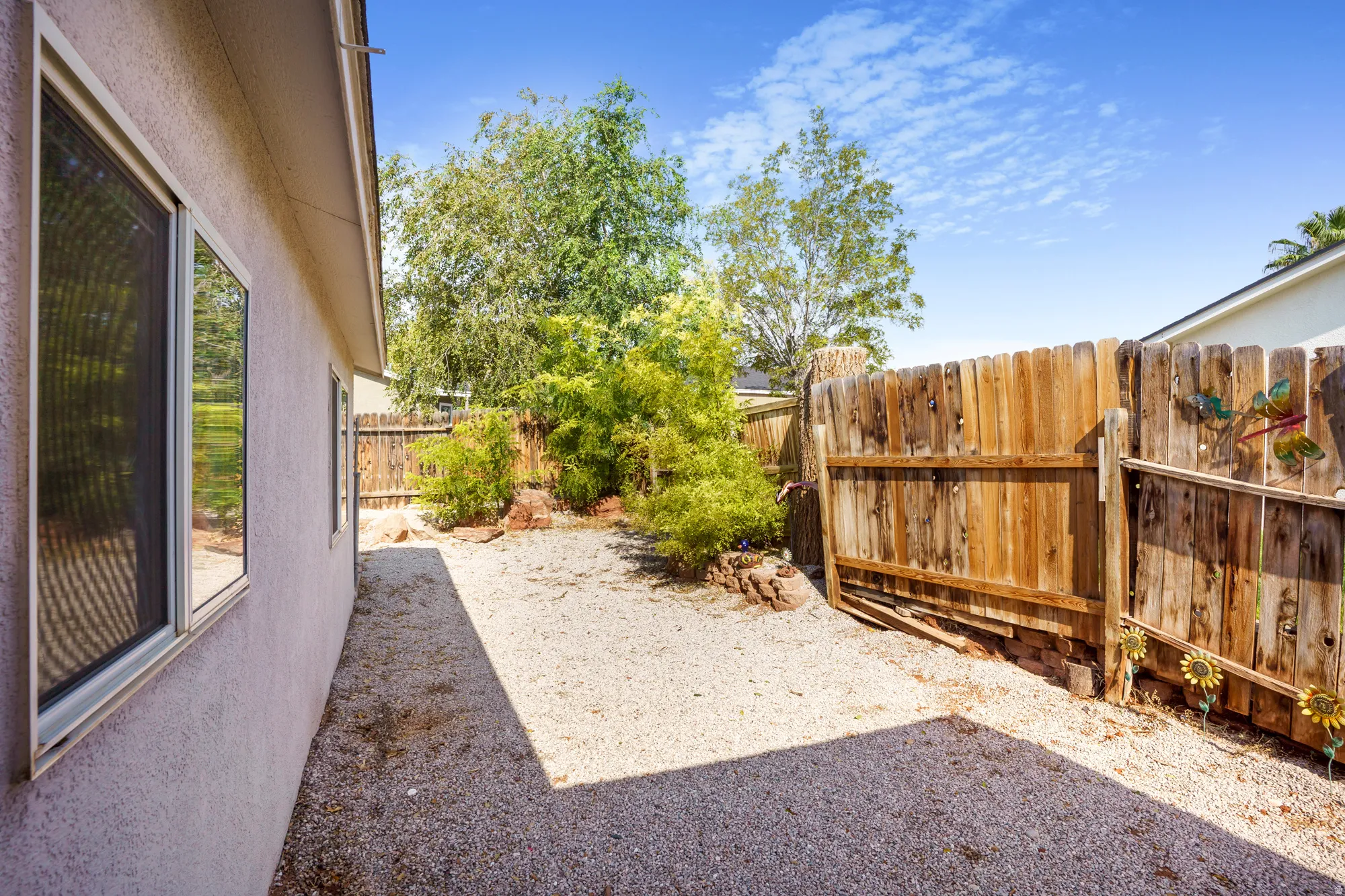 Stucco exterior with multiple windows, gravel ground cover, and a wood privacy fence