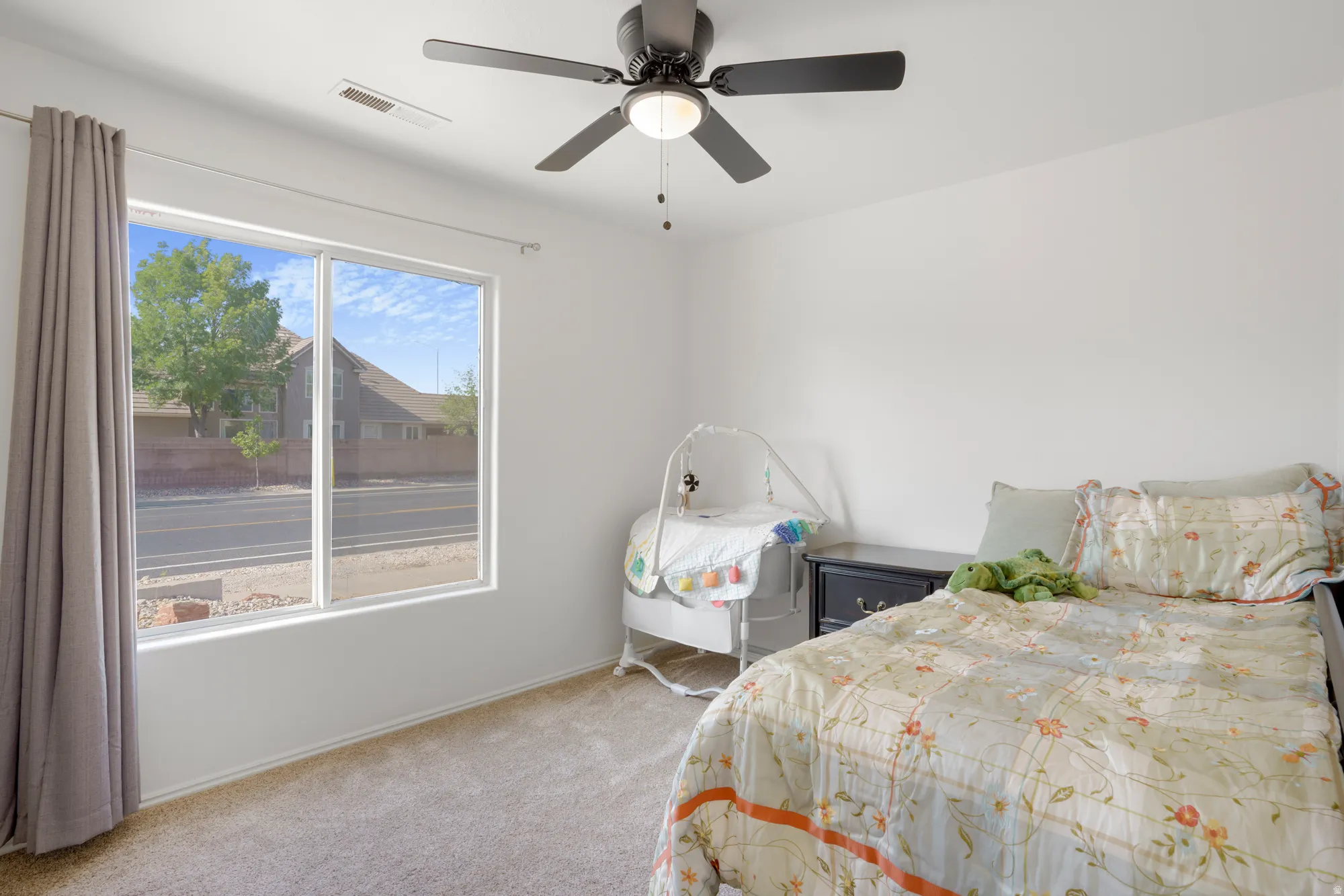 Bright secondary bedroom featuring expansive sliding glass doors with natural light, neutral carpeting, ceiling fan with integrated lighting, and ample closet storage