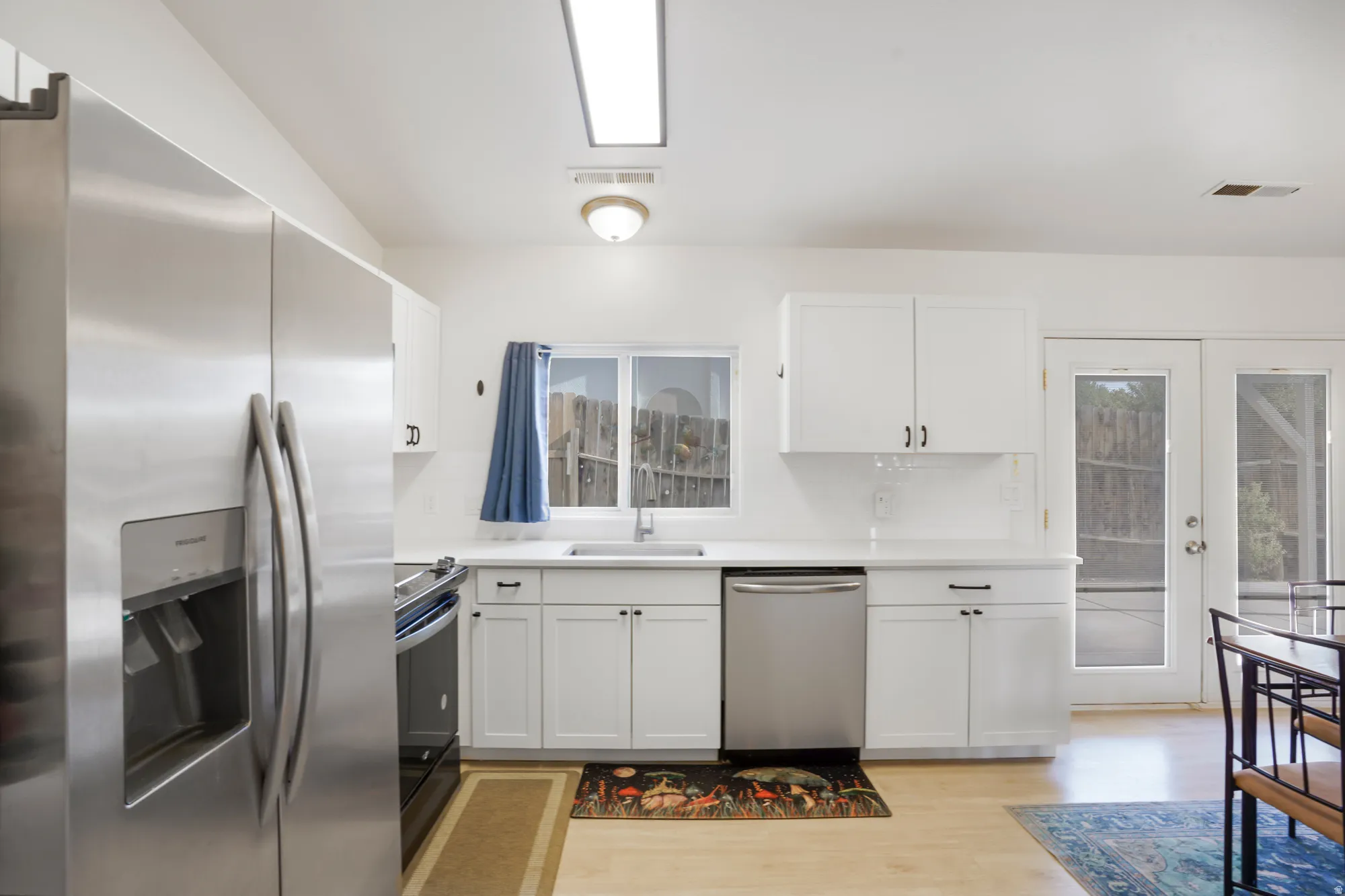 Stainless steel appliances, white cabinetry, light wood-finish flooring, white countertops, and a subway tile backsplash