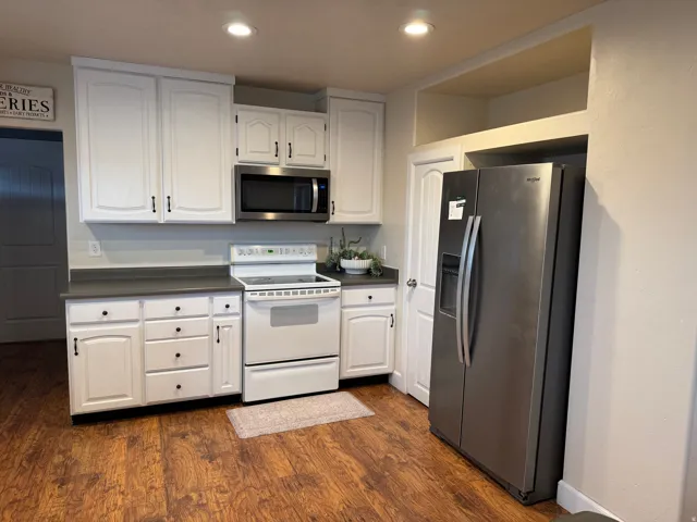White cabinetry with black hardware, stainless steel microwave, wood-finish flooring, and recessed lighting