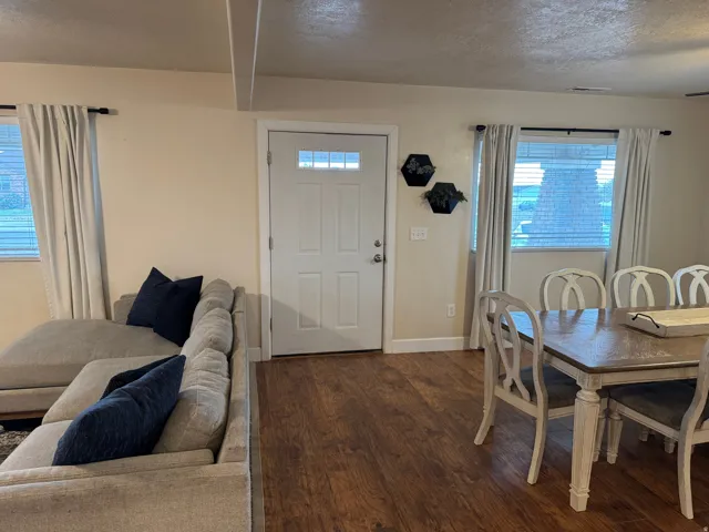 Wood-finish flooring throughout, white paneled entry door with transom lites, and multiple windows with blinds