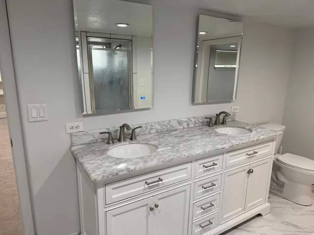 Dual sink vanity with stone-finish countertop, brushed nickel faucets, and white shaker-style cabinetry
