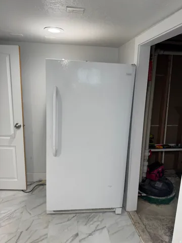 White refrigerator, recessed ceiling lighting, white interior door, marble-look floor tiles, white wall paint