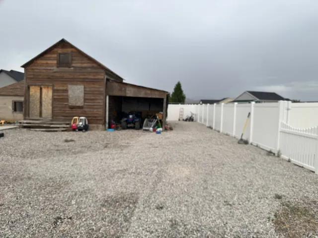 Gravel yard with a white panel fence and a wooden outbuilding