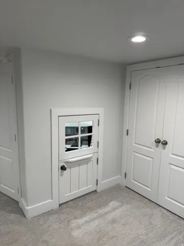 Light gray walls, recessed ceiling lighting, white panel doors with bronze-finish hardware, and light gray patterned carpeting