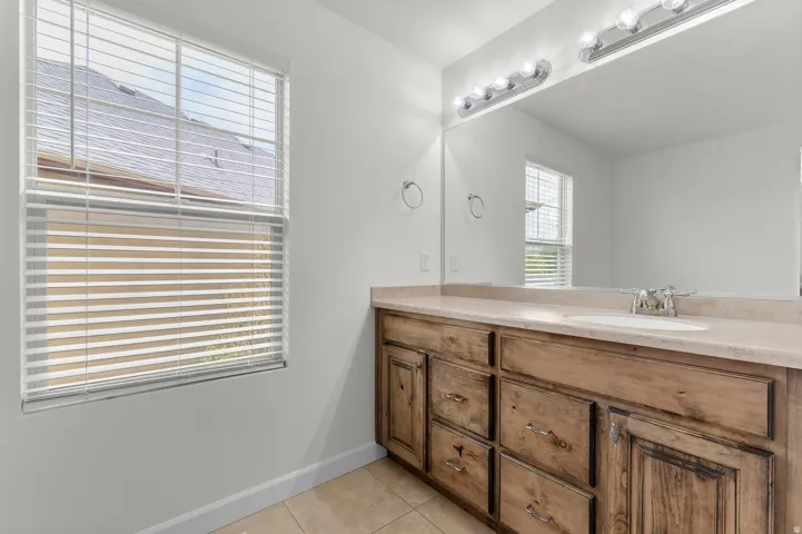 Wood-finish vanity with an integrated sink, stone-finish countertop, and full-width mirror with overhead lighting