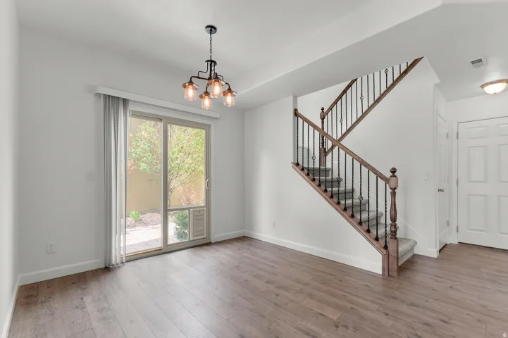 Wood-finish flooring, staircase with dark wood banister and wrought iron spindles, sliding glass patio door, modern industrial chandelier, and a paneled entry door