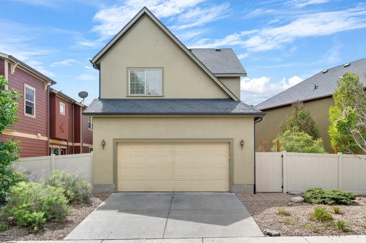 Stucco exterior with an attached garage, a paved driveway, and mature landscaping