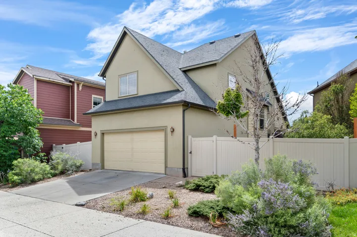 Stucco exterior with a pitched roof, attached garage, concrete driveway, and front landscaping