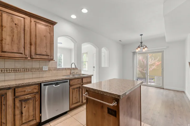 Kitchen featuring wood cabinetry, stainless steel dishwasher, stone countertops, and tile backsplash