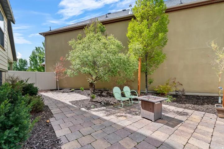 Paver patio with a built-in fire pit, surrounded by mature landscaping and a privacy fence