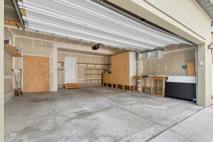 Attached garage with concrete flooring, built-in cabinetry, and open shelving