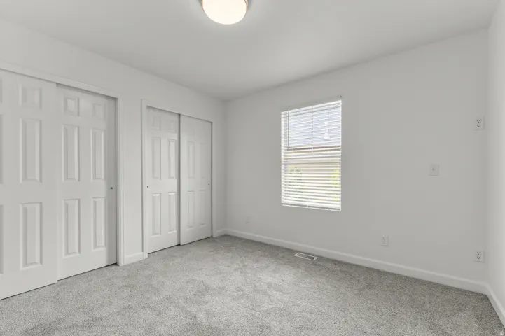 Bright bedroom featuring neutral carpeting, large casement window with plantation shutters, and dual closet doors providing ample storage