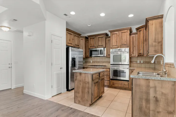 Kitchen featuring wood-finish cabinetry, stainless steel appliances, a center island, granite countertops, and tile flooring