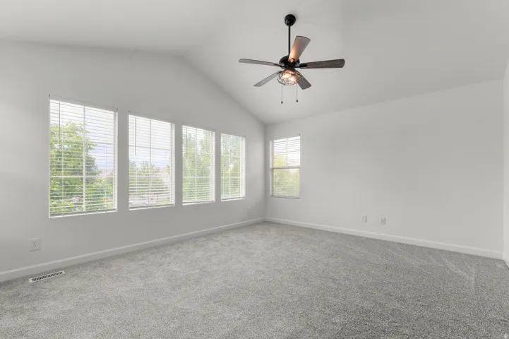 Vaulted ceiling with a ceiling fan, plush gray carpeting, and multiple windows with blinds