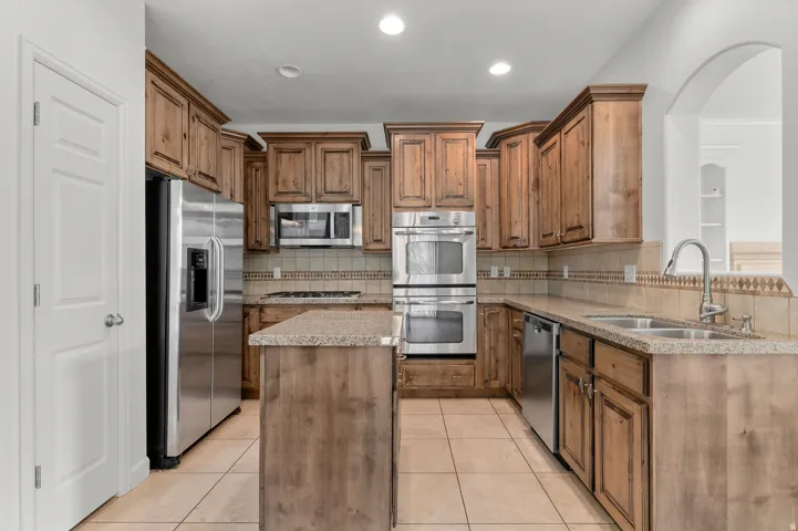 Kitchen featuring wood cabinetry, stainless steel appliances, a center island, tiled flooring, and an archway