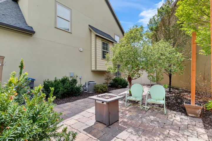 Paved patio area featuring a built-in fire pit, mature trees, and established shrubbery