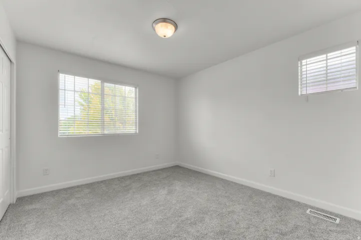 Plush carpeting, neutral wall tones, and multiple windows with included blinds