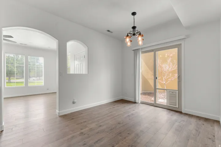 Wood-finish flooring throughout, arched doorway, sliding glass door, modern ceiling light fixture, and an arched wall cutout