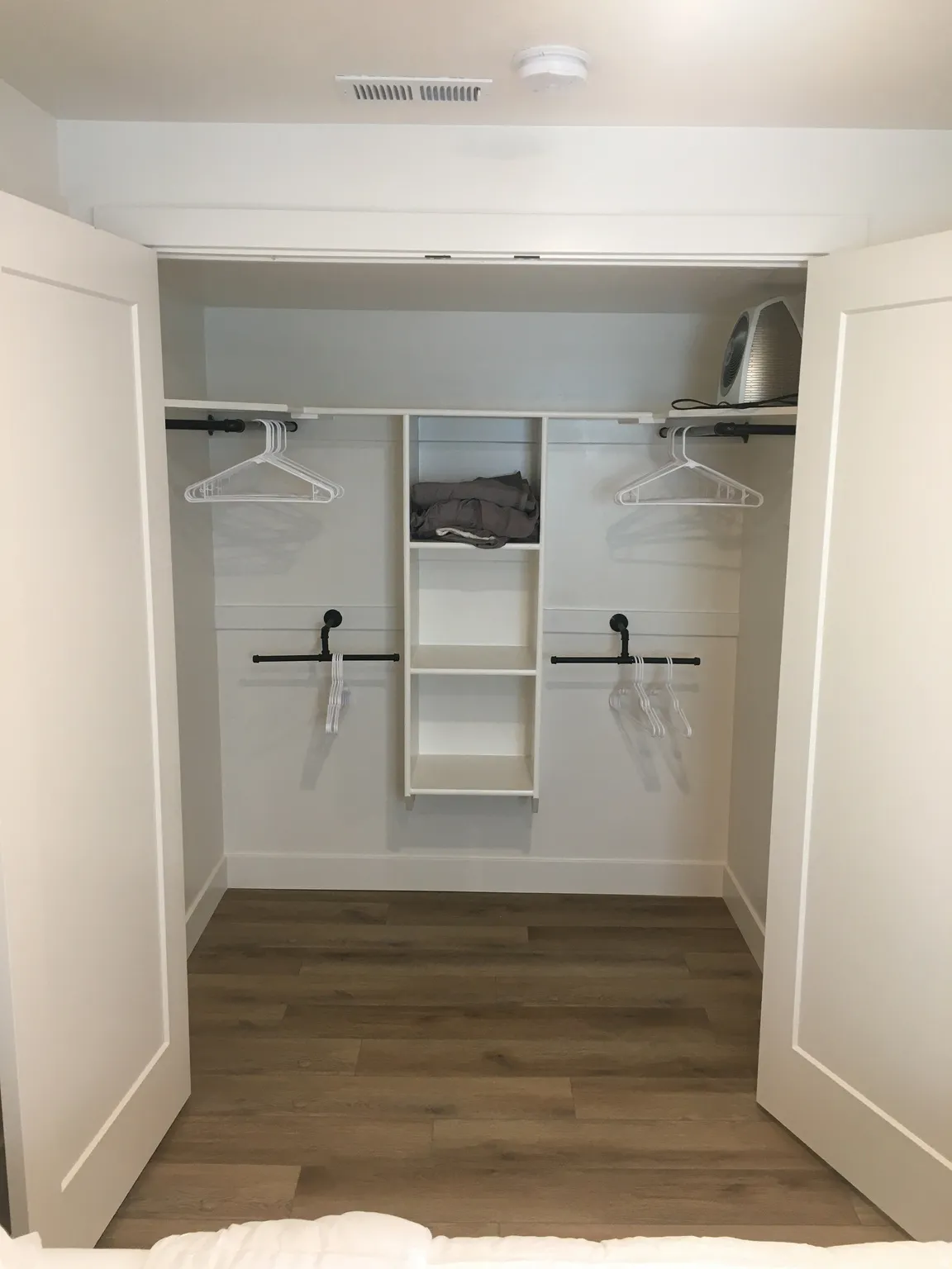 Walk-in closet with wood-finish flooring, white walls, built-in shelving, and black metal hanging rods