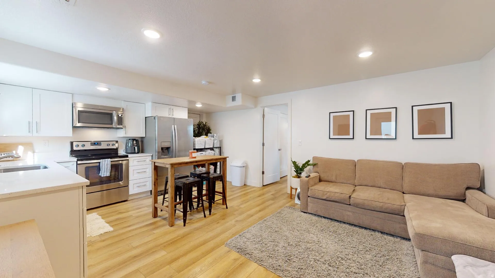 Kitchen featuring stainless steel appliances, white cabinetry, and light-toned wood-finish flooring