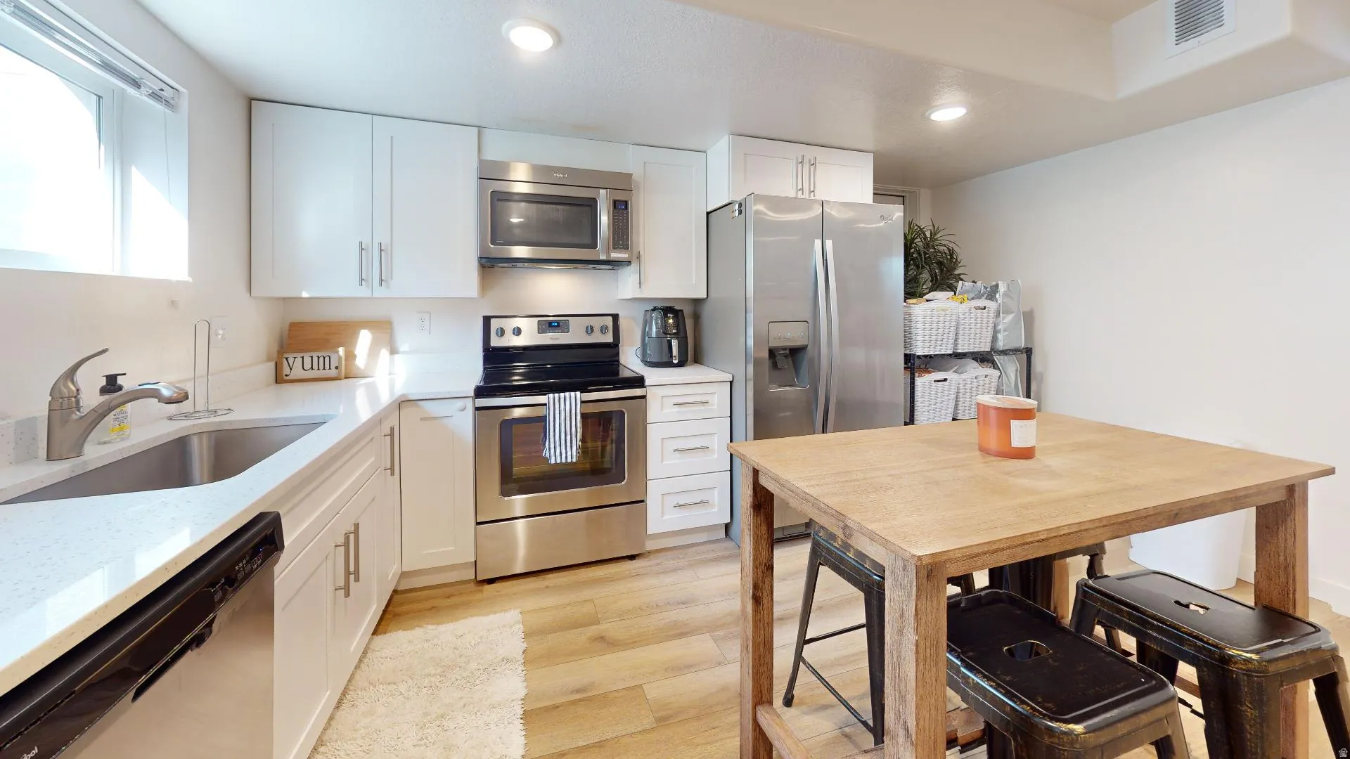 White shaker cabinetry, stainless steel appliances, light wood-finish flooring, and solid surface countertops