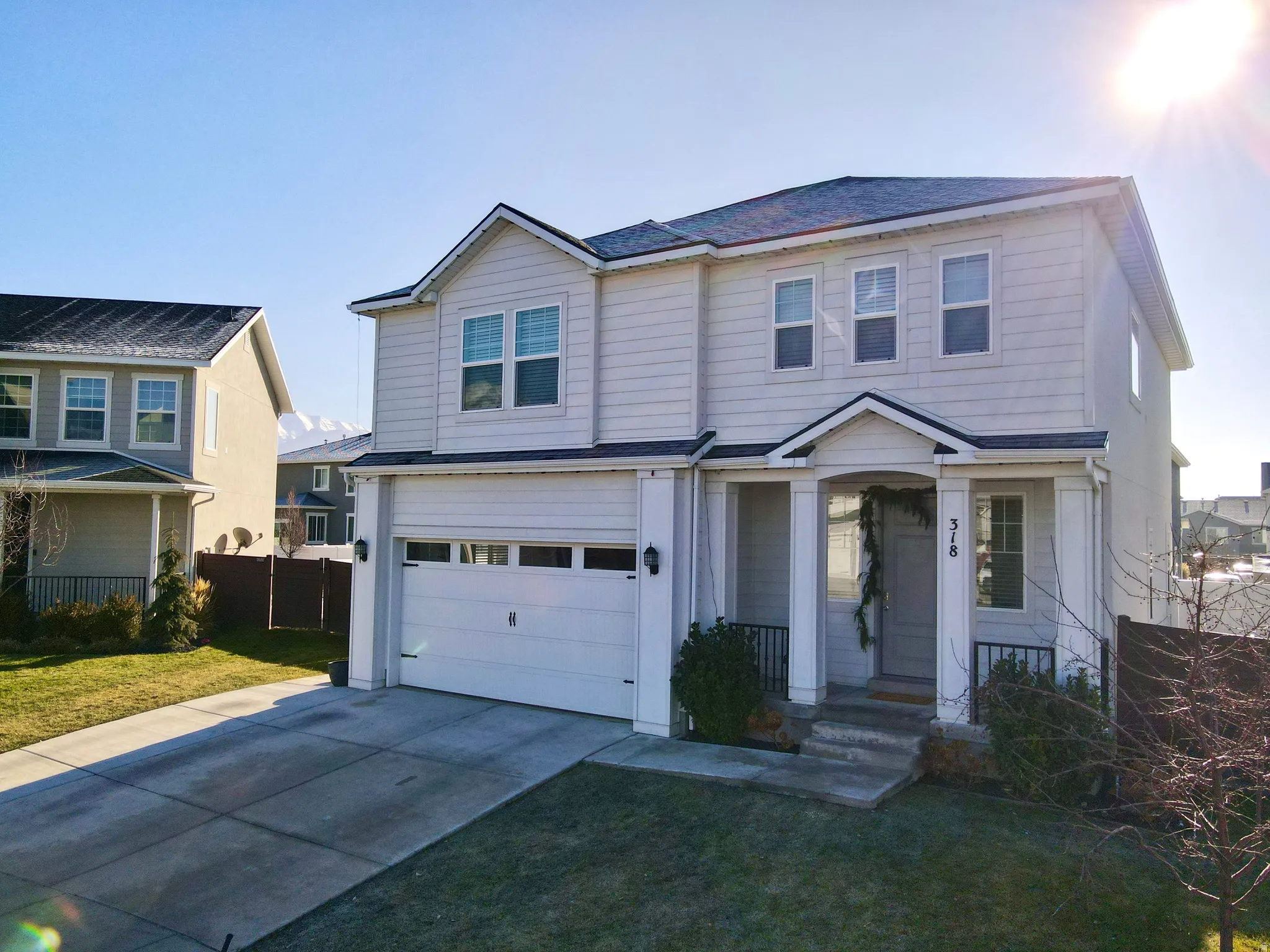 Two-story residence featuring light-colored siding, a covered front porch with pillar supports, an attached garage, a paved driveway, and a partially fenced yard