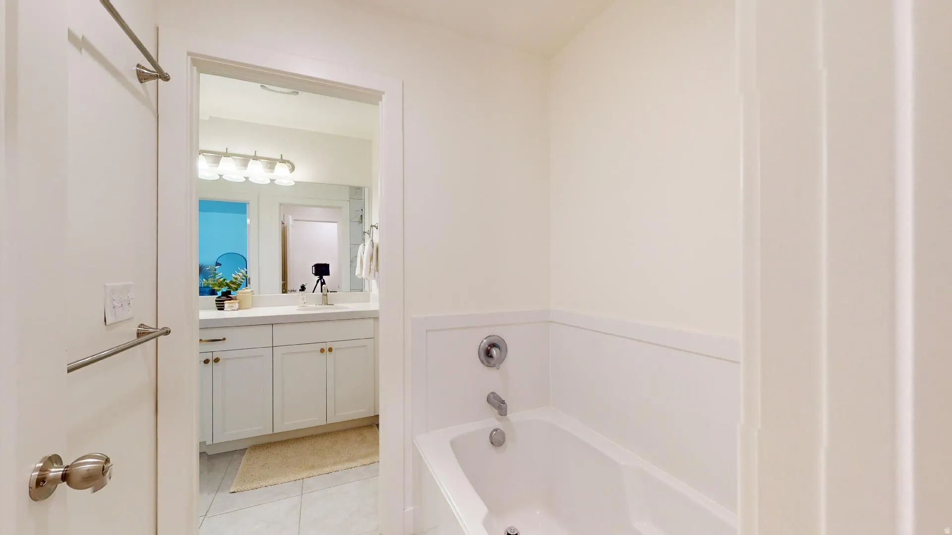 White built-in bathtub with chrome fixtures, white wainscoting, and a neutral wall finish