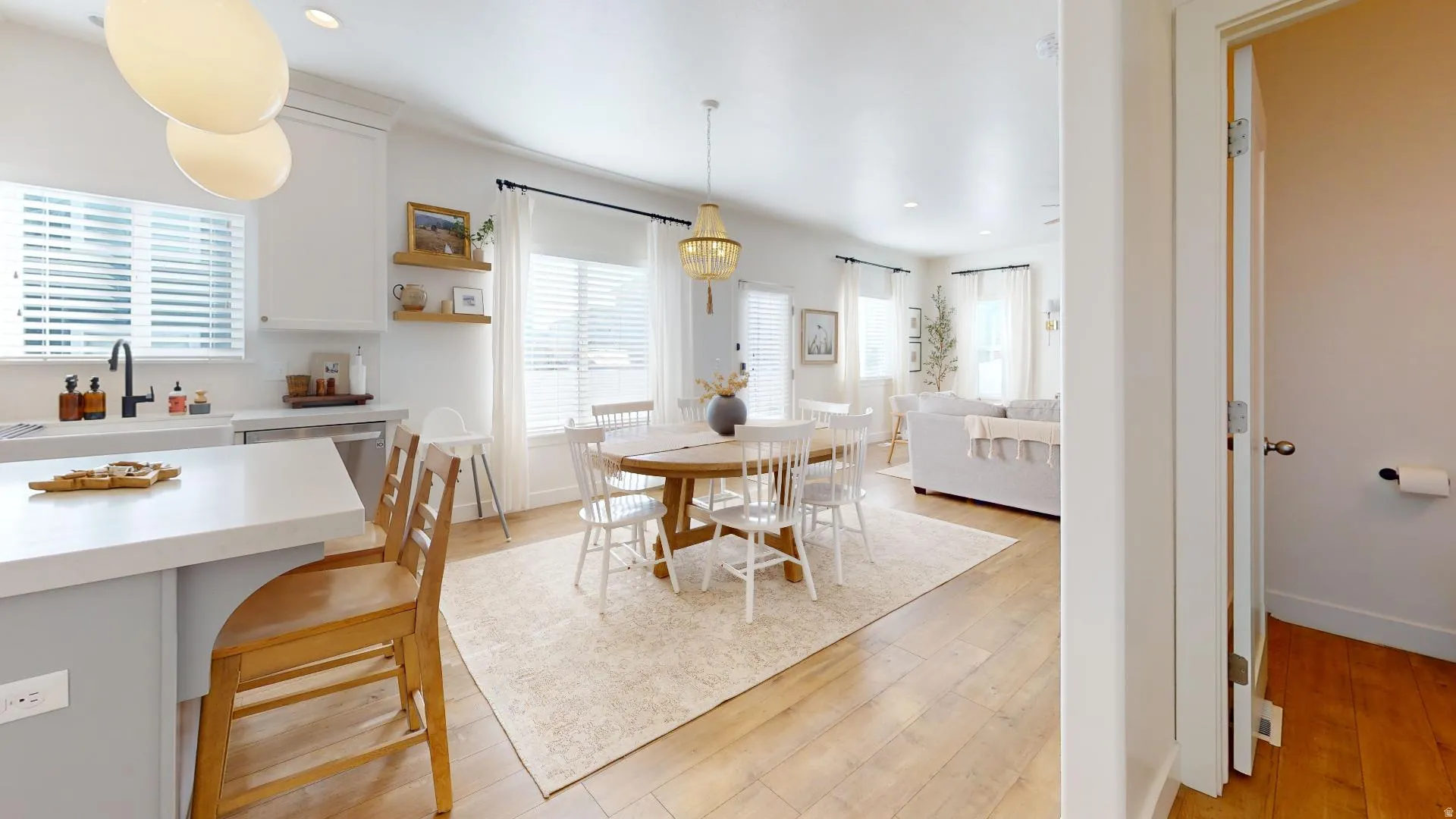Open-concept living area featuring wood-finish flooring, white cabinetry, a kitchen island with seating, a dining area with a chandelier, and a living room space