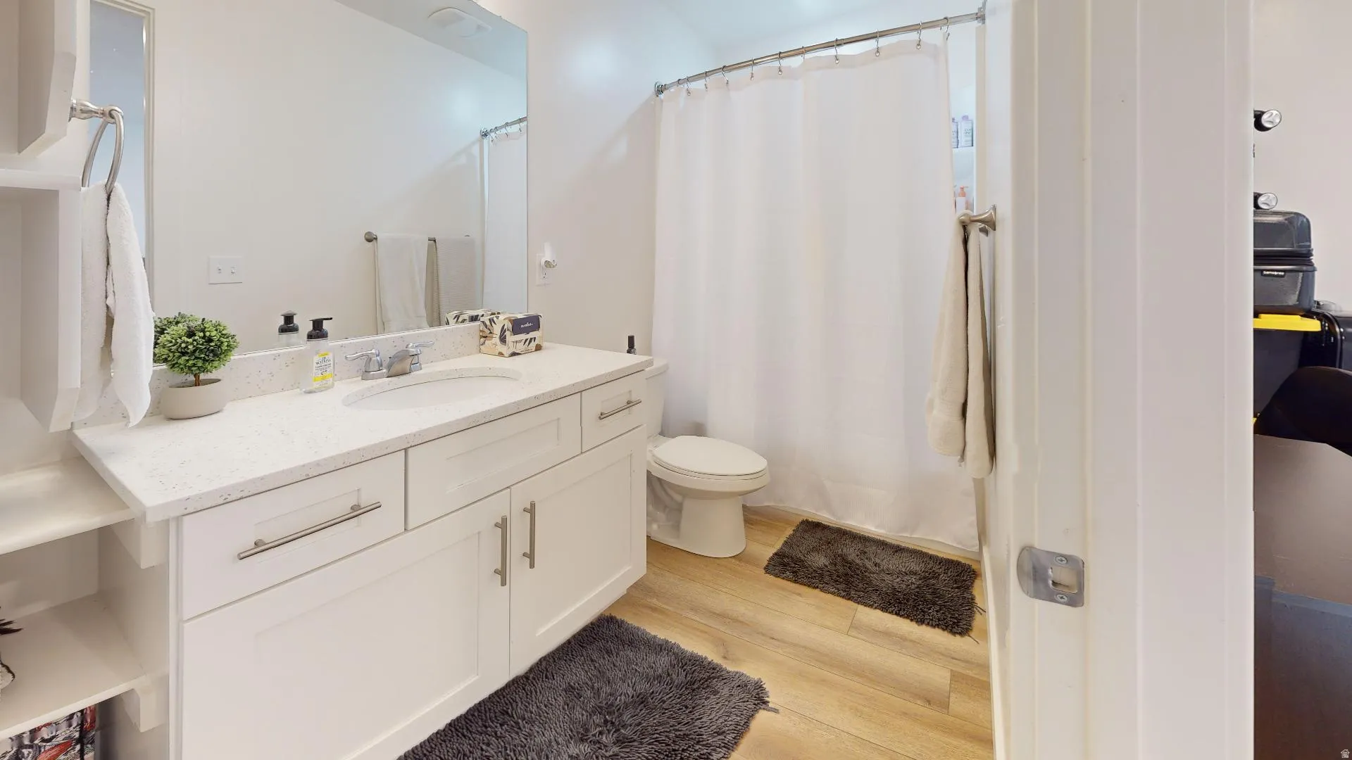 White vanity with a single basin sink, light-colored countertop, built-in shelving, and wood-finish flooring