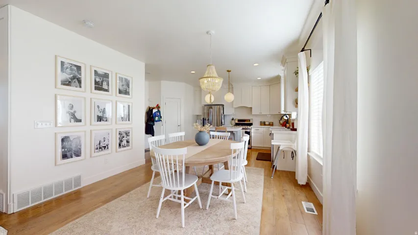 Open-concept dining area with wood-finish flooring, a contemporary chandelier, and a large window with blinds