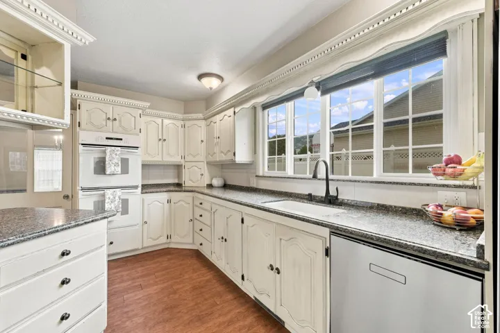 Kitchen featuring white cabinetry, stone countertops, wood-finish flooring, a built-in double oven, and a stainless steel dishwasher