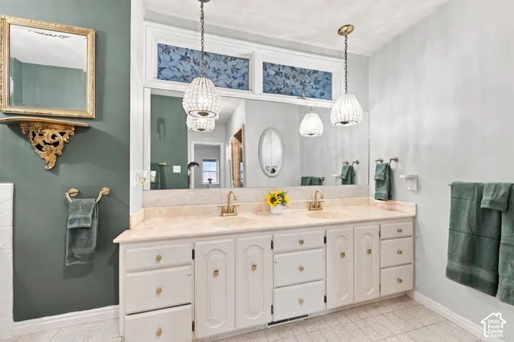 Double vanity with integrated sinks and brass-finish fixtures, complemented by crystal pendant lighting and an ornate mirror