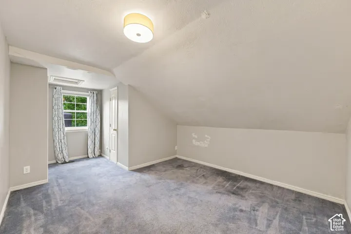 Carpeted room with a window, sloped ceiling, and a ceiling-mounted light fixture