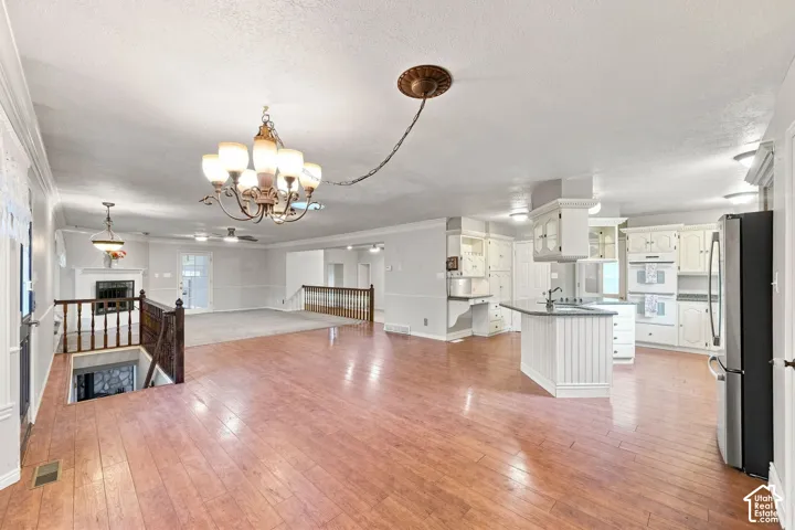 Wood-finish flooring, white cabinetry, kitchen island with sink, stainless steel refrigerator, and a fireplace with mantel