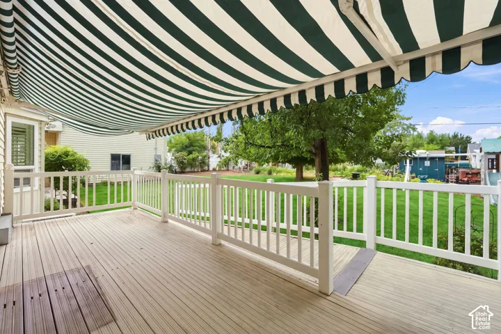 Expansive deck featuring wood-finish flooring, white railing, and a striped retractable awning