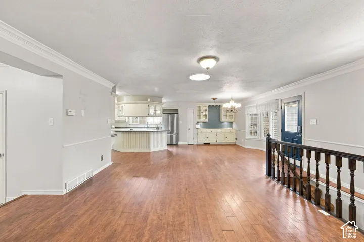 Open-concept living area with wood-finish flooring, crown molding, and a kitchen featuring white cabinetry and stainless steel appliances