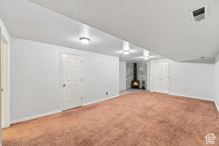 Spacious room featuring carpeting, recessed lighting, and a corner stone-clad wood-burning stove
