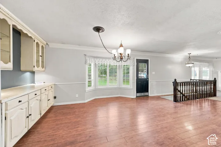 Hardwood-style flooring, white built-in cabinetry with glass display doors, bay window with plantation shutters, dark wood-finish staircase railing, and a dark entry door with glass inserts