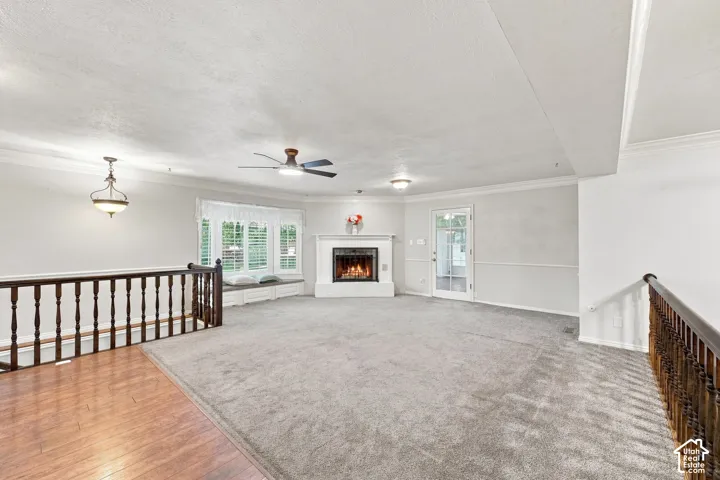 Carpeted living area featuring a fireplace, bay window with built-in seating, ceiling fan, and crown molding