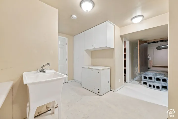 Laundry area featuring a utility sink with dual-handle faucet, white cabinetry, and overhead lighting